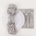 Silver satin napkin tied on a white plate with cutlery on a gray placemat