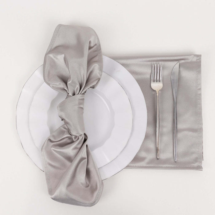 Silver satin napkin tied on a white plate with cutlery on a gray placemat
