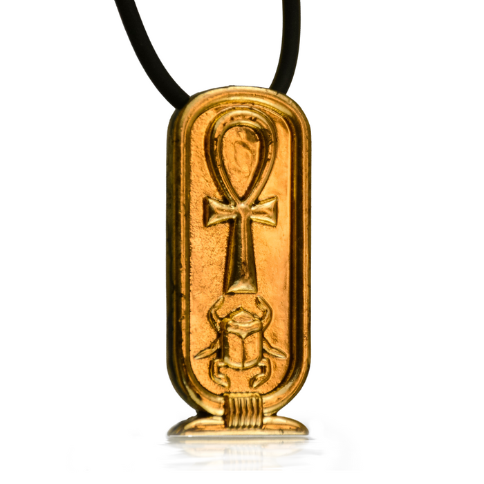 Golden cartouche oval-shaped pendant with ankh loop symbol on the top front face and a scarab beneath it. On a black necklace with white background, slight reflection of pendant beneath it.