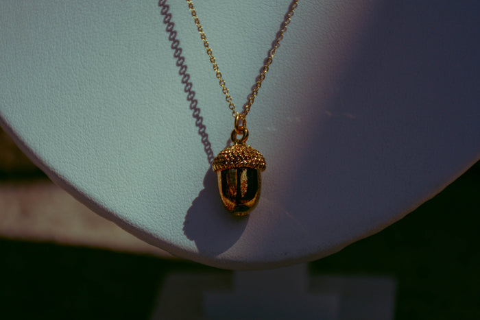 Gold dainty acorn necklace on background with creative lighting. Purple, pink, red, black, and green.