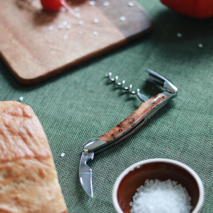 Forge de Laguiole Corkscrew Juniper, close-up of shiny steel and grained wood handle on green cloth.