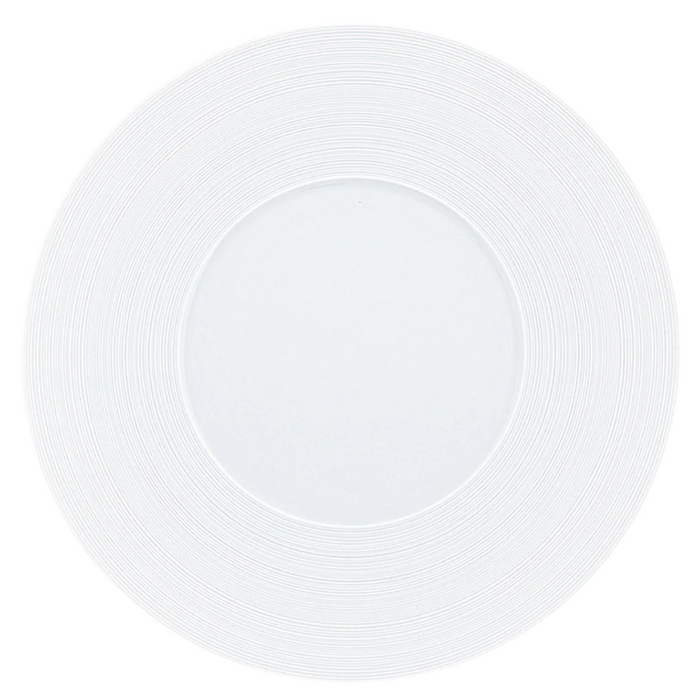 A JL Coquet Hemisphere Dinnerware Satin White plate, viewed from above, features a subtle circular textured pattern engraved on its porcelain rim.
